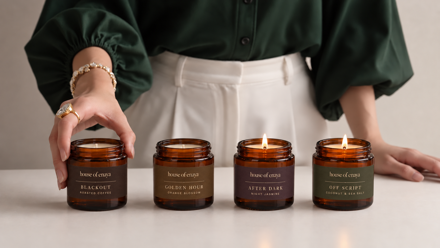 Enaya in a green shirt arranging the four House of Enaya 80ml candles on a cream table