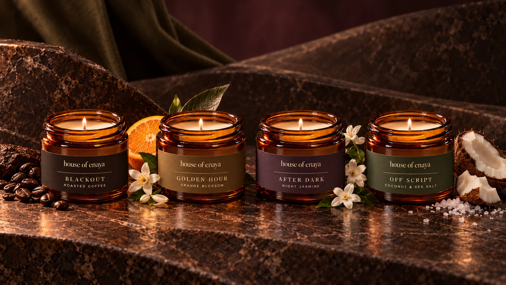 Four House of Enaya candles surrounded by coffee beans, orange blossom, jasmine, coconut and sea salt